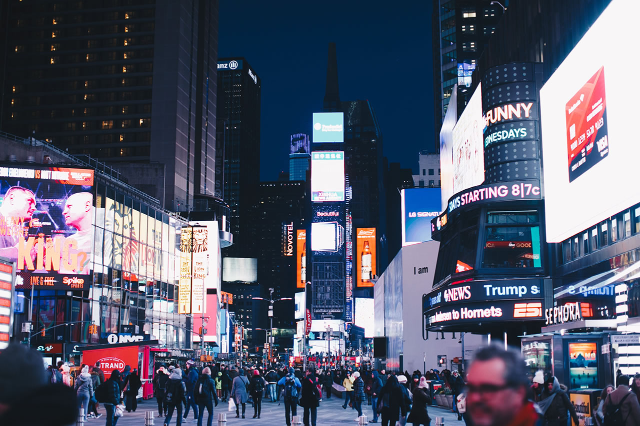Image of Times Square at night. The street is filled with people, and the billboards are all lit up.